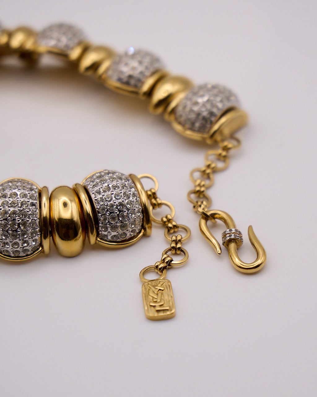 Primo piano dei cristalli a pavé e dei raccordi dorati della collana, con chiusura e targhetta YSL.