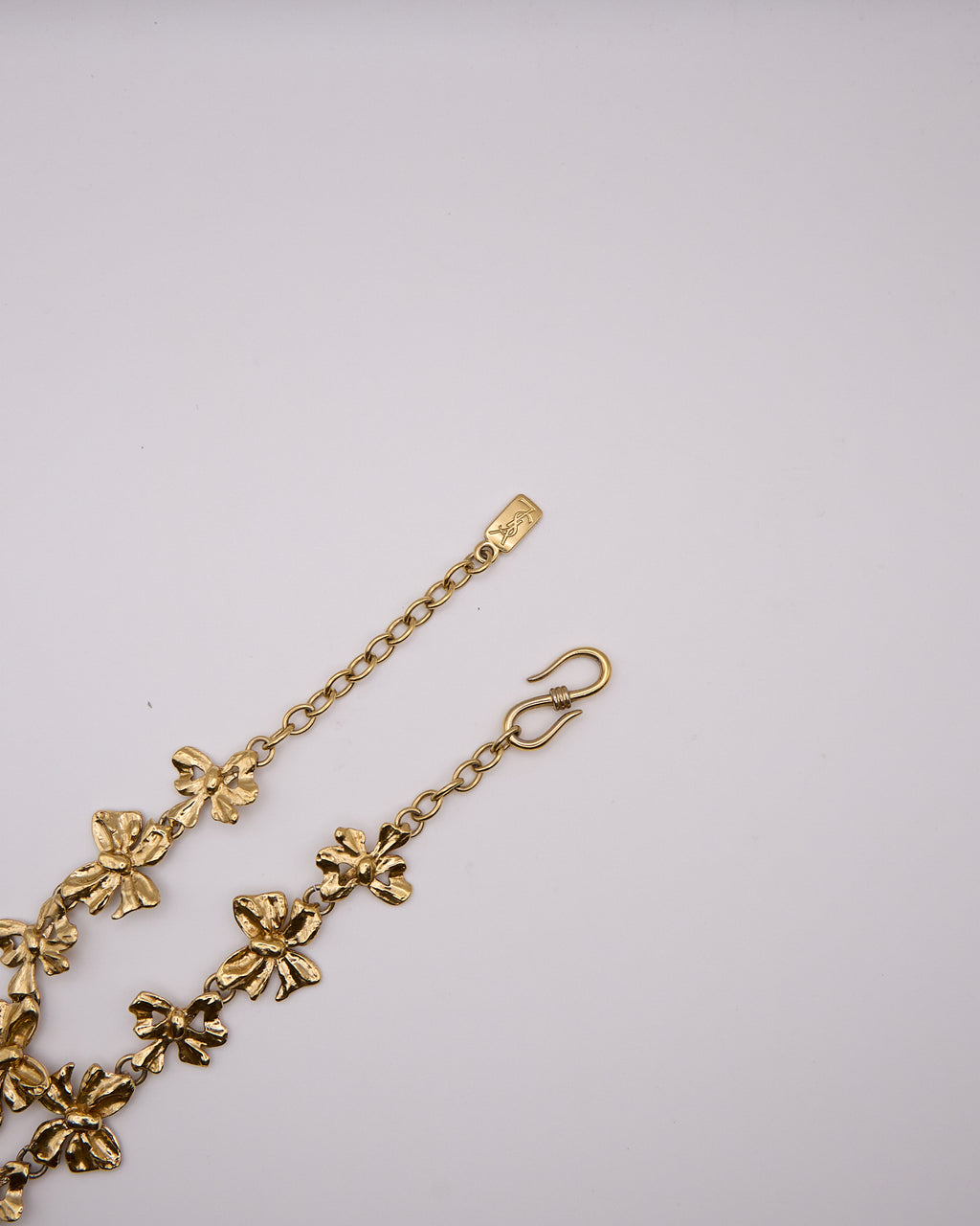 Dettaglio dei fiocchi dalla superficie increspata, della catenella con monogramma YSL e della chiusura a S.