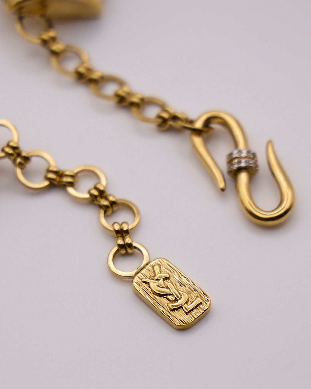 Targhetta rettangolare con monogramma YSL accanto alla chiusura a S decorata con cristalli.