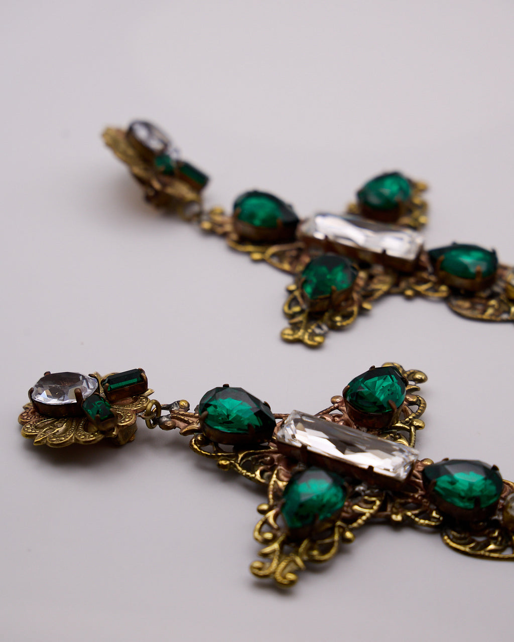  Dettaglio dei cristalli verdi e trasparenti sfaccettati e delle volute traforate degli orecchini a croce.