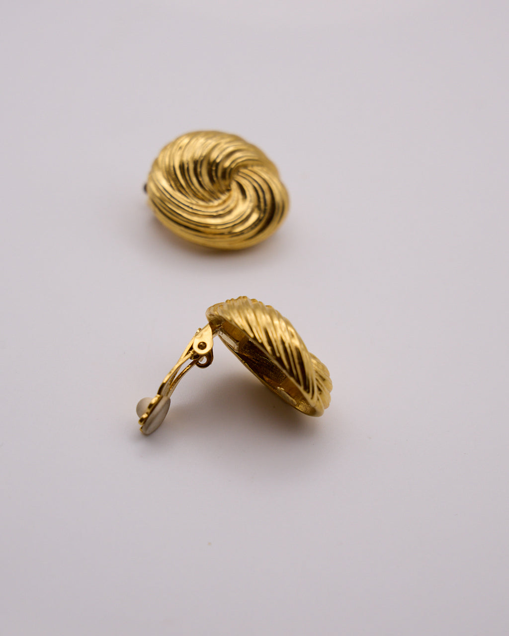 Orecchini dorati con motivo a spirale, uno visto frontalmente e uno di lato con chiusura a clip aperta.