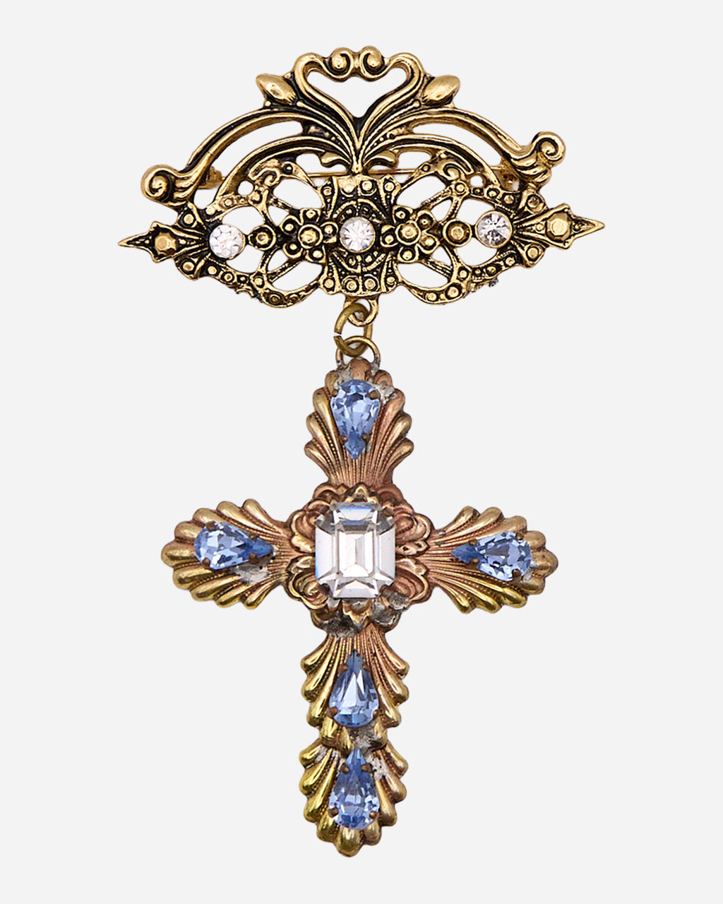 Spilla vintage dorata con parte superiore traforata e croce pendente ornata da cinque cristalli azzurri a goccia e un cristallo centrale trasparente.